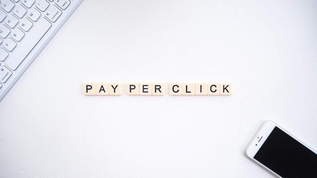 Image de lettres formant les mots "Pay Per Click" avec un clavier et un smartphone en arrière-plan, symbolisant le marketing PPC.